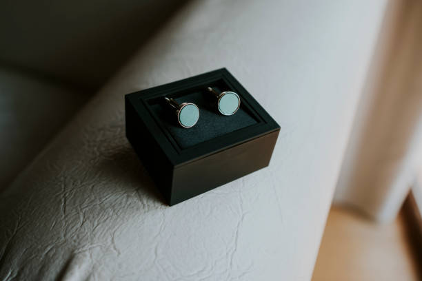Round black men's cufflinks in their box. Close-up detail of the twins, horizontal photography in black and white tones.