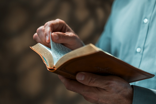 Hands of a man praying in solitude with his Bible (Christian image, shallow focus).