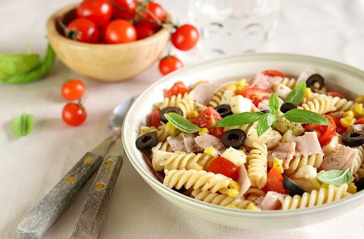 Italian food concept. Summer pasta salad with mozzarella, tomatoes, prosciutto, basil ad olives. Healthy food. Overhead view.
