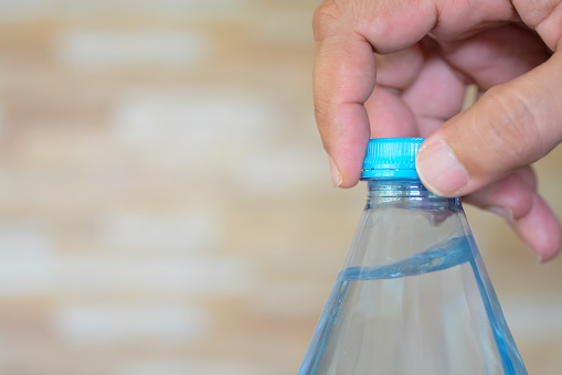 hands delicately twist open the cap of a refreshing bottle of water, ready to quench a thirst.