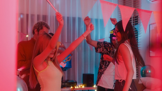 Diverse group of friends dancing moving rhythmically in good mood at colorful house party at night. Multicultural friends having fun together college house party concept.