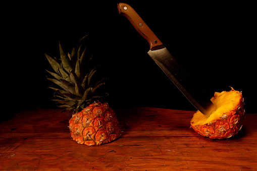 Knife and halved pineapples on wooden table