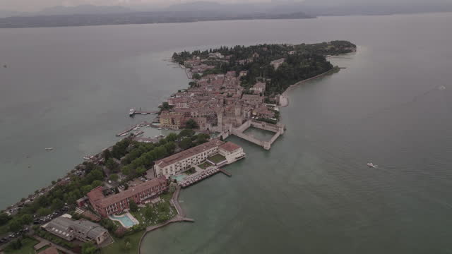 Drone shot of Simione Italy looking over the old fortress on a grey day with boats around in the water near the lake LOG