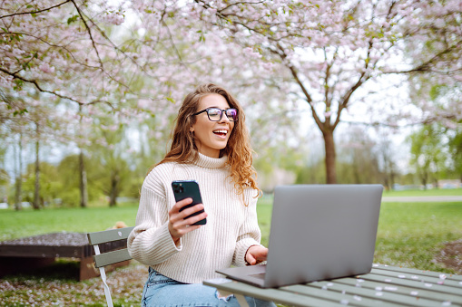 Happy woman sitting with laptop and phone sitting at a table outdoors . Concept for education, business, shopping, blog or freelance.