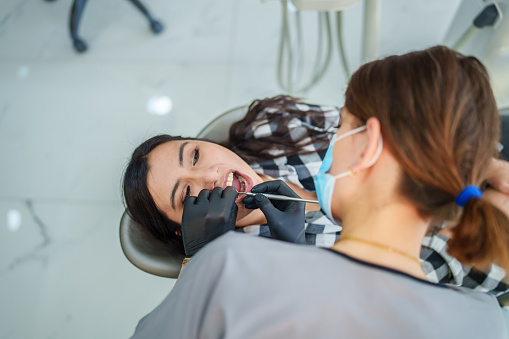 Part of a series: A female dentist is performing the implant treatment on a woman patient lying in the dental chair.