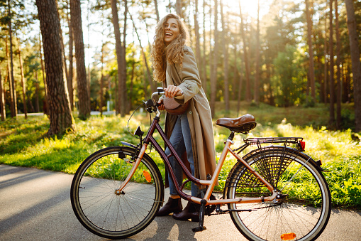 Young woman in stylish clothes rides a bicycle in a sunny park. Active lifestyle.