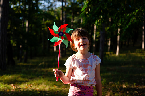 Cute little girl holding a pinwheel in nature and looking at the camera.