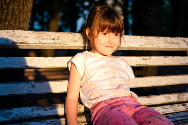 Cute happy girl sitting on bench in park during sunny summer day