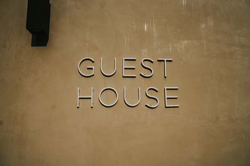 Neon sign saying Guest House on plain yellowish wall. \nIlluminated sign off, with modern typography.