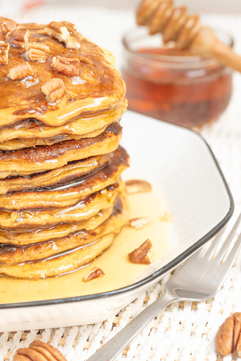 A stack of home-fried sweet potato pancakes, topped with chopped pecans and drizzled with warm honey maple syrup on a plate. Southern-style crepes for brunch, breakfast or dessert, for a delicious moment.