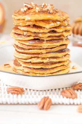 A stack of home-fried sweet potato pancakes, topped with chopped pecans and drizzled with warm honey maple syrup on a plate. Southern-style crepes for brunch, breakfast or dessert, for a delicious moment.
