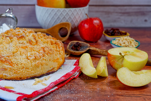 Freshly baked apple pie on a rustic kitchen worktop with ingredients and kitchen utensils.