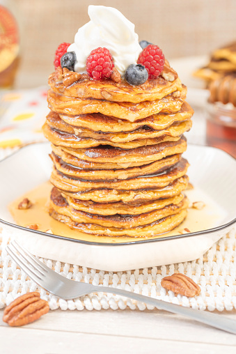 A stack of home-fried sweet potato pancakes, topped with chopped pecans, fruits, whipped cream and drizzled with warm honey maple syrup on a plate. Southern-style crepes for brunch, breakfast or dessert, for a delicious moment.