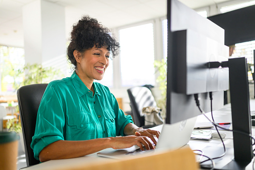 Front view of smiling mature businesswoman working on laptop in modern office.