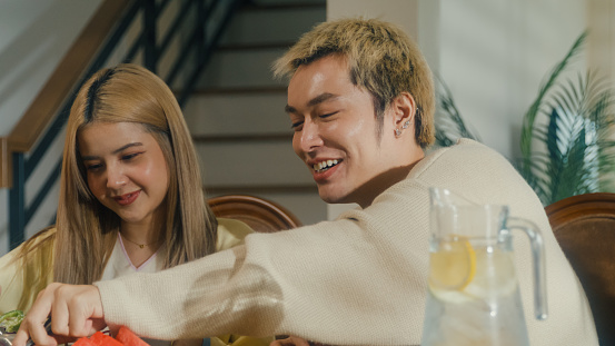 Group of young Asian people preparing and having fun sitting at dining table at home. Multicultural friends having fun together college house party concept.