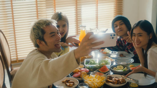 istock Group of young Asian people using mobile phone taking selfie and having fun sitting at dining table at home. Multicultural friends enjoying spending together college house party. 2009999605