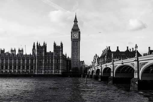 Monochromatic landscape shot of big Ben overlooking the river Thames with an overcast shadow and tourists overlooking the scenery on the bridge