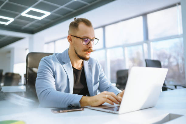 istock Young man wearing glasses working with laptop while sitting at his working place. Business, technology, study. 2010022135