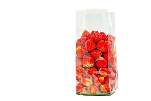 Isolated image of strawberry in cleared plastic bag on white background, bedding the strawberry with banana leaf in the plastic bag.
