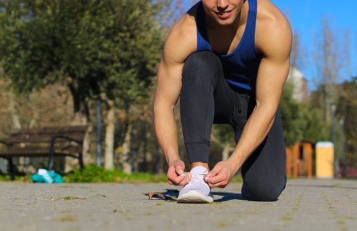 Caucasian man smiling tying his sneakers kneeling outside, sports dress, getting ready for sports, side view, with copy space. Lifestyle concept