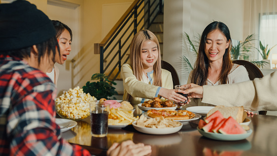 Group of young Asian people preparing and having fun sitting at dining table at home. Multicultural friends having fun together college house party concept.