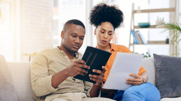 istock Black couple, tablet and documents with financial crisis on living room sofa discussing mortgage payment. Home, African man and woman together with paperwork in debt, finance issue or money problems 2010047005