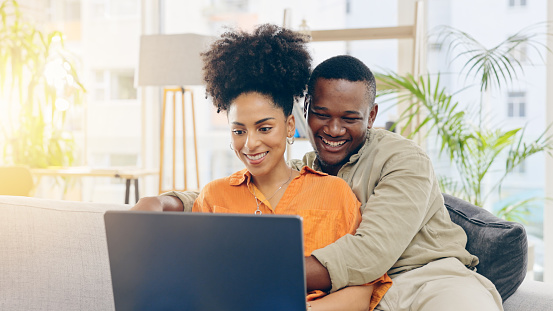 Couple, laptop and smile with hug on sofa in home living room, online browsing or web scrolling. Interracial, computer and happiness of black man and woman bonding on couch in lounge on social media.
