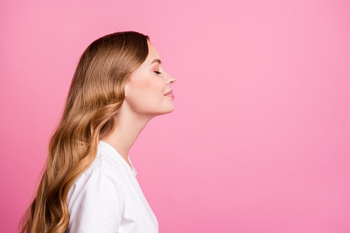 Side profile photo of adorable nice girl with curly hair dressed white t-shirt smell fragrant perfume isolated on pink color background.