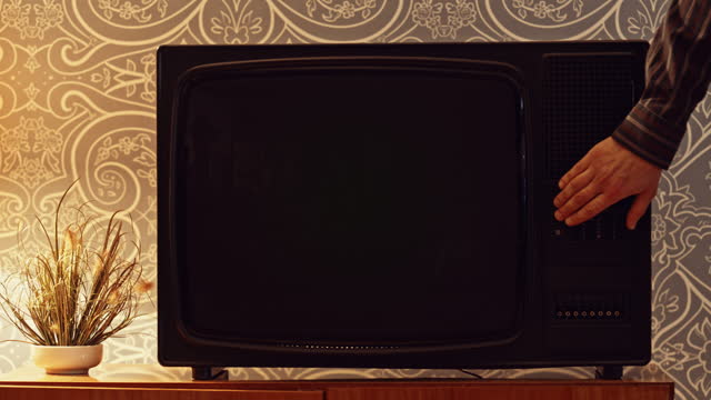 LD Male hand turning on an old TV set with a green screen