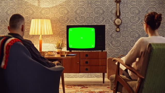 DS Man and woman sitting in the living room and man watching the old tv set with a green screen