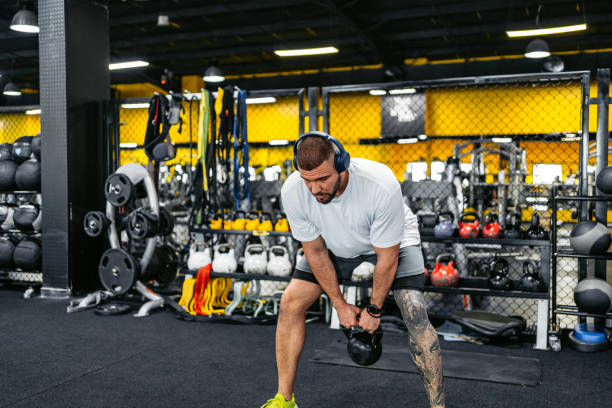 jeune homme s’entraînant avec un kettlebell tout en écoutant de la musique dans la salle de sport - hand weight audio photos et images de collection