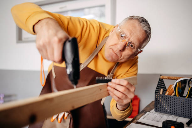 istock Mature man working at home in garage using drill for making wooden shelf 2010138846