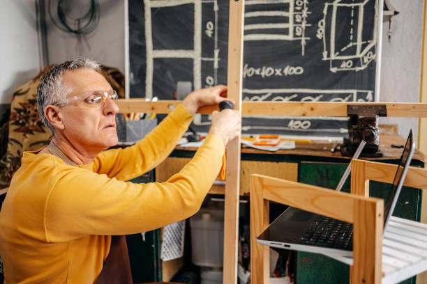 istock Mature man working at home in garage using drill for making wooden shelf 2010139373