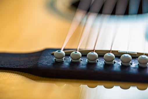 Extreme close up view of steel strings and bridge of an acoustic guitar.