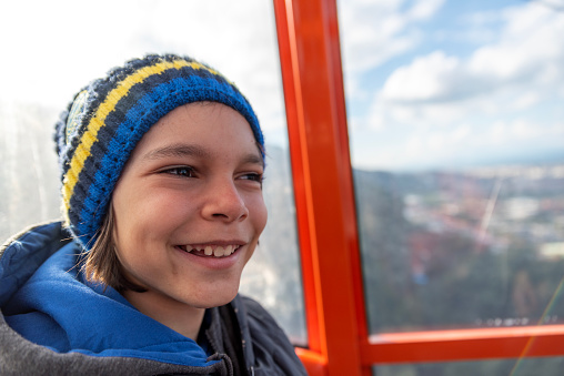 Portrait of happy cute boy wearing colorful woolen hat in front of glass inside cable car cabin