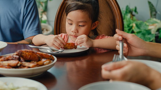 Closeup of young Asian family eating food and having fun sitting at dining table at backyard outside home. Multi-generation family enjoying spending together concept.