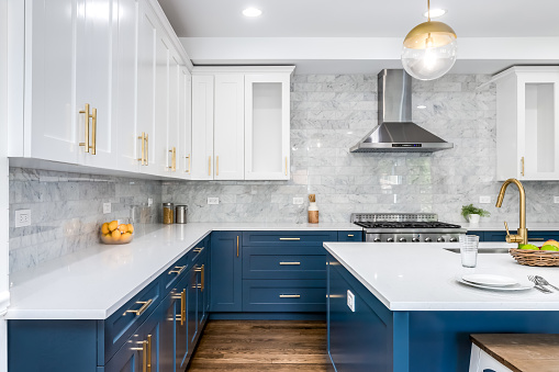 A luxurious white and blue kitchen with gold hardware, stainless steel appliances, marble subway tile backsplash, and white marble granite countertops. No brands or labels.