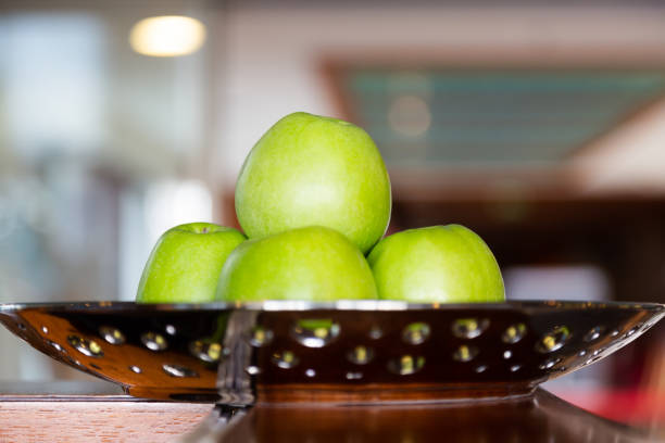 Green large fresh apples on golden plate in kitchen. Close up front shot.
