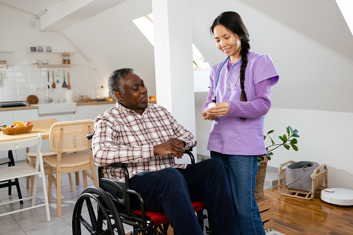 African American senior man in a wheelchair having a visit from his home caregiver.