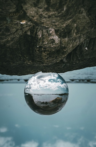 perspective shot of a crystal ball overlooking the ocean sitting on a rock bed in Cornwall's countryside