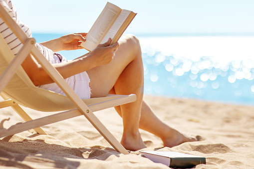 Woman sitting with book in the chaise lounge on the sea beach. Tourism and vacation concept.