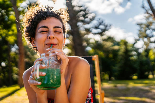 mujer joven bebiendo jugo verde en el bar al aire libre - drinking straw drinking juice women fotografías e imágenes de stock