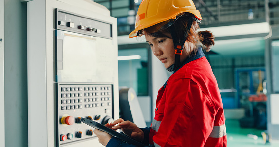 Professional Asian female industrial engineers operating machine keypad in manufacturing factory. Engineering and sustainable production plant concept.