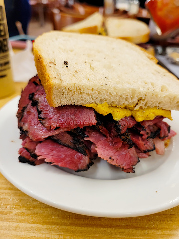 Delicious stacked pastrami sandwich on toasted rye, served on a white plate, restaurant