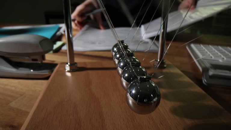 Pendulum with iron balls on table with documents in office closeup 4k movie