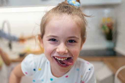 Portrait of a cute Caucasian girl with milk moustache, in the kitchen