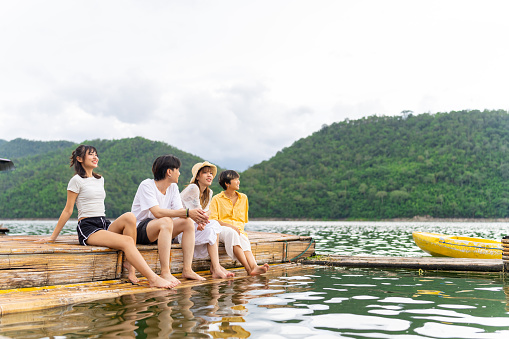 Group of Young Asian man and woman enjoy and fun outdoor lifestyle travel nature forest mountain on summer holiday vacation. Happy generation z people friends relaxing together on lake house balcony.