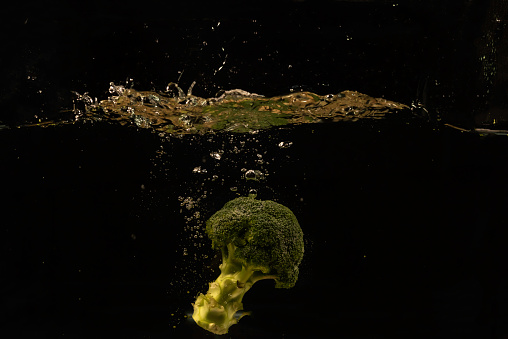 Photo of a vegetables and fruits dropped under water with splash on black background