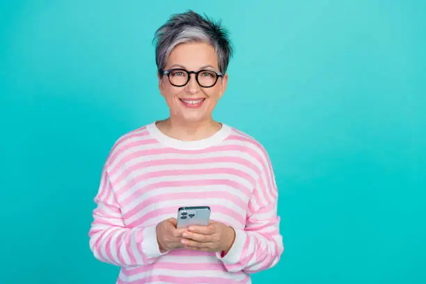 Photo of excited cute lady wear striped sweater spectacles chatting modern device empty space isolated turquoise color background.