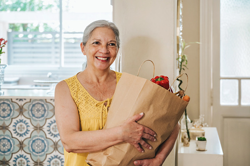 smiling happy senior woman holding shopping bag with groceries in kitchen